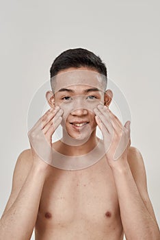 Portrait of young asian man with problematic skin and hyperpigmentation smiling at camera, applying cream on his face