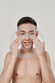 Portrait of young asian man with problematic skin and hyperpigmentation smiling at camera, applying cream on his face photo