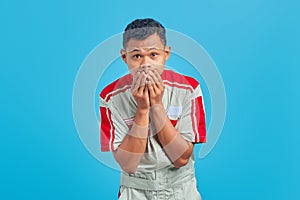 Portrait of young Asian mechanic covering his mouth with hands with surprised expression on blue background