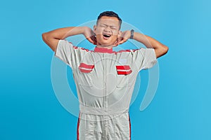 Portrait of young Asian mechanic feeling sleepy with mouth open over blue background