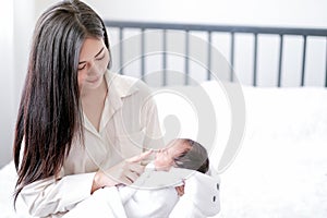 Portrait of young asian mother has fun with her newborn baby by finger playing to the baby on white bed