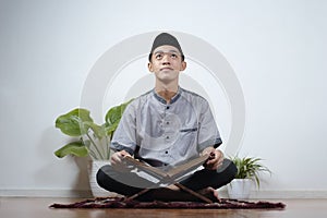 Portrait of Young Asian Muslim man looking up reading holy Qur`an on Ramadan Kareem