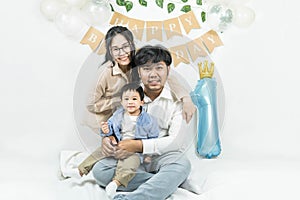 Portrait of young asian parents keep in arms, hugging child kid baby boy,celebrating first birthday holiday party on a minimal