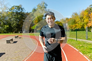 Portrait of a young Asian sportsman runner in black sportswear running in the stadium and smiling at the camera