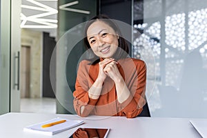 Portrait of young Asian successful business woman, female worker at workplace inside office smiling and looking at