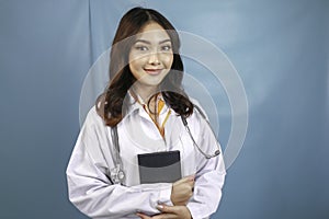 Portrait of a young Asian woman doctor, a medical professional is smiling and holding notes isolated over blue background