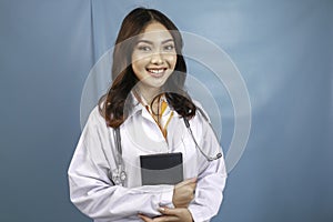Portrait of a young Asian woman doctor, a medical professional is smiling and holding notes isolated over blue background