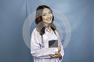 Portrait of a young Asian woman doctor, a medical professional is smiling and holding notes isolated over blue background