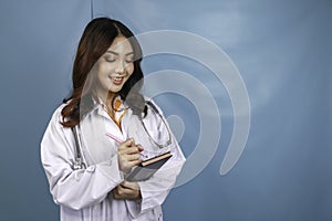 Portrait of a young Asian woman doctor, a medical professional is smiling and holding notes isolated over blue background