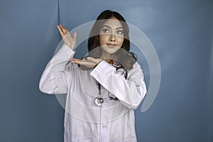 Portrait of a young Asian woman doctor, a medical professional is smiling and pointing upward at a copy space isolated over blue