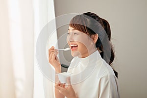 Portrait of young Asian woman eating yogurt behind the window