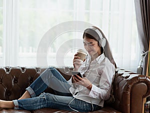 Young Asian woman enjoy listening to music with headphones and holding a hot cup of coffee  happy and relaxing time