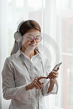Young Asian woman enjoy listening to music with headphones while holding mobile phone, happy and relaxing time