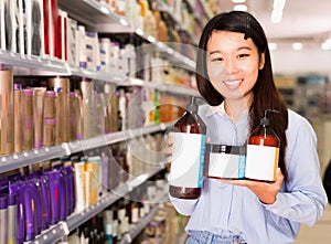 Portrait of young Asian woman holding kit of hair care products in supermarket