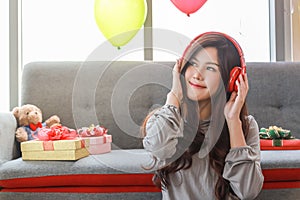 Portrait of young asian woman listening the music with red headphone in living room with gift boxes and balloon party photo