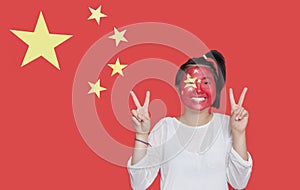 Portrait of young Asian woman with painted face gesturing peace sign against Chinese flag