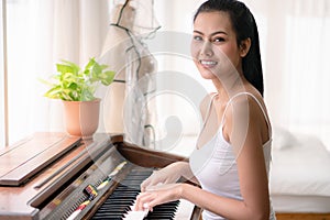 Portrait of young asian woman playing piano in living room at home