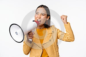 Portrait of young asian woman protester, screaming in megaphone and protesting, standing confident against white