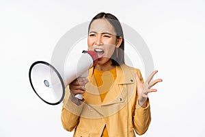 Portrait of young asian woman protester, screaming in megaphone and protesting, standing confident against white