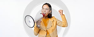 Portrait of young asian woman protester, screaming in megaphone and protesting, standing confident against white