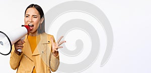 Portrait of young asian woman protester, screaming in megaphone and protesting, standing confident against white