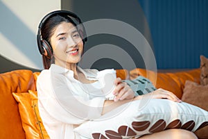 Portrait of a young asian woman using mobile phone and earphones to listening to music or online chatting at home