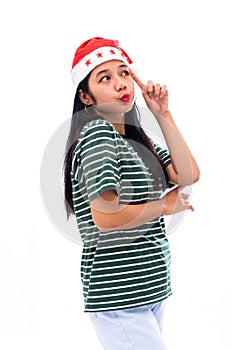 Portrait of young asian woman wearing a santa hat and wearing casual clothes lifting a finger near the head looks thinking