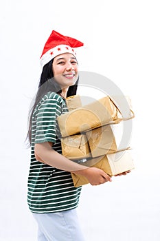 Portrait of a young Asian woman wearing a santa hat and wearing casual clothes lifting a pile of gifts