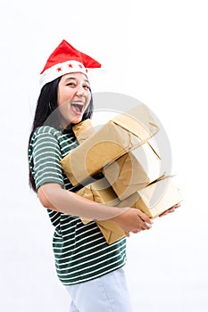 Portrait of a young Asian woman wearing a santa hat and wearing casual clothes lifting a pile of gifts with surprise face