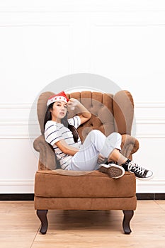 Portrait of young Asian woman wearing a Santa hat and wearing casual clothes sitting on a brown sofa