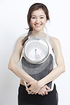 Portrait of young Asian woman with weight scale against white background