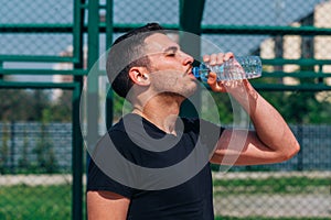 Portrait of a young athlete drinking water on a basketball court on a nice sunny day while wearing a black t-shirt