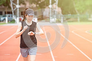 Portrait of young athlete runner woman running in the running track and she looking to her smart watch.