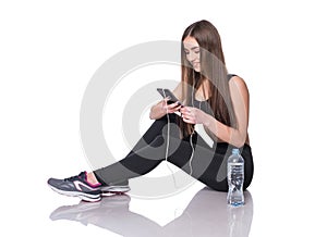 Portrait of a young athlete woman listening to music with earphones over white background. Attractive fitness girl chatting