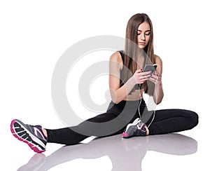 Portrait of a young athlete woman listening to music with earphones over white background. Attractive fitness girl chatting on sma
