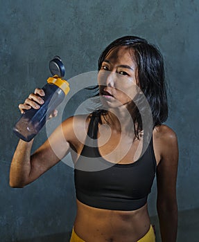 Portrait of young athletic and fit Asian Korean woman in fitness top holding drinking water bottle posing cool in bad girl defiant