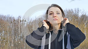 Portrait of young athletic girl doing exercise in the morning outddors in the park wearing dark sportwear and wireless