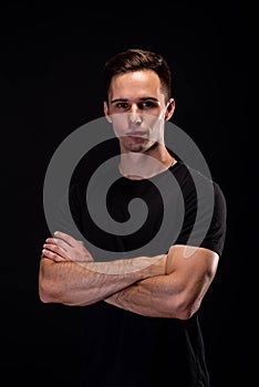 Portrait of a young athletic man in a black T-shirt on a black background. Young beautiful sporty man