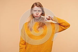 Portrait of young attaractive woman with loose foxy hair puffing out her cheeks and frowning eyebrows while looking at camera,