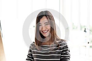 Portrait of young attractive asian creative woman or designer smiling and looking at camera in modern office feeling confident