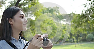 Portrait of young attractive asian woman photographer taking photos in a summer park.