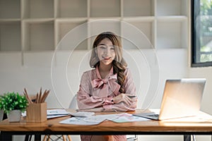 Portrait of young attractive asian woman with relaxing while sitting at her office desk, smiling and looking at camera