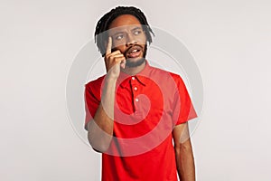 Portrait of young attractive bearded man with dreadlocks wearing red casual style T-shirt, thinking, has new idea, looking way