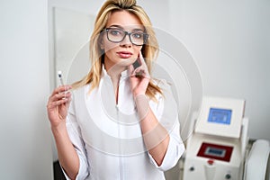 Portrait of young attractive beautician doctor with syringe in hand. Cosmetologist holding medical tools. Practician in photo