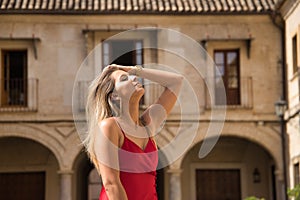 Portrait of young, attractive, blonde woman in an elegant red party dress sensually touching her hair in the city. Concept beauty