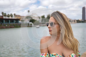 Portrait of young, attractive, blonde woman with sunglasses, looking towards a river. Concept beauty, fashion, trend, travel