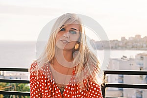 Portrait of a young attractive blue-eyed blonde woman with long hair looking into the camera and smiling, wearing a red