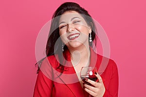 Portrait of young attractive brunette woman with glass of white wine in hands, lady posing isolated over pink studio background,