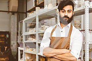 Portrait of a young attractive businessman craftsman with a beard and mustache in his workshop.. Posing arms crossed