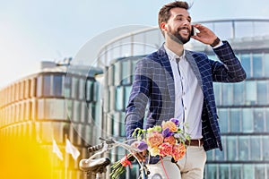 Portrait of young attractive businessman holding boquet of flowers while talking on smartphone